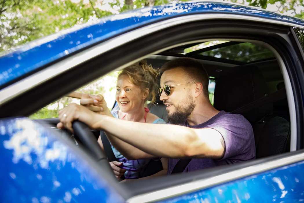 Mies ja nainen istuvat auton kyydissä innostuneen näköisinä.