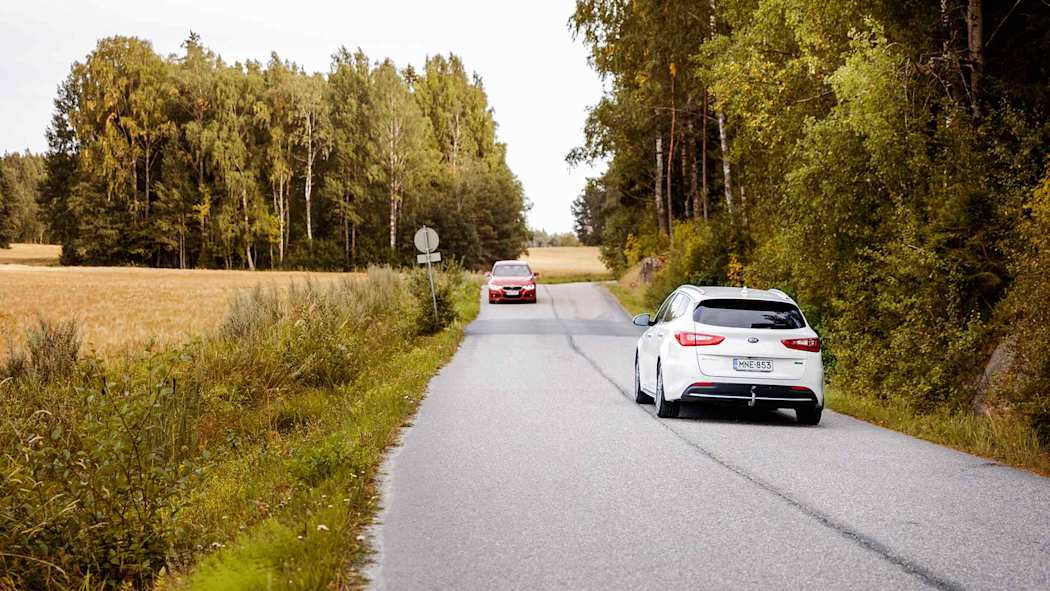 Kaksi autoa vastakkaisilla kaistoilla kapealla maantiellä metsän reunassa syyssäässä
