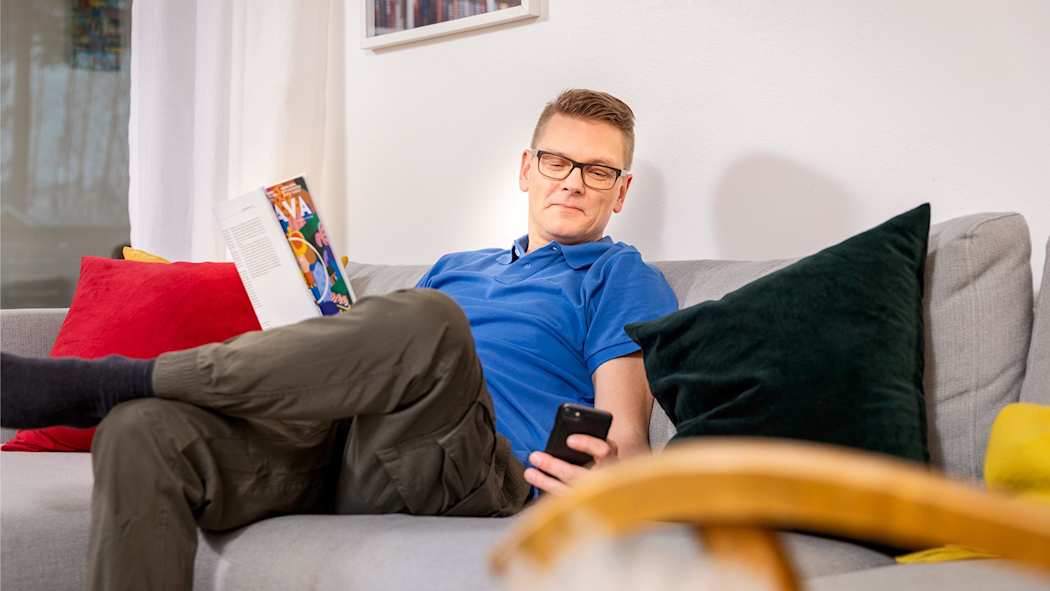 Mies istuskelee sohvalla ja selaa puhelintaan