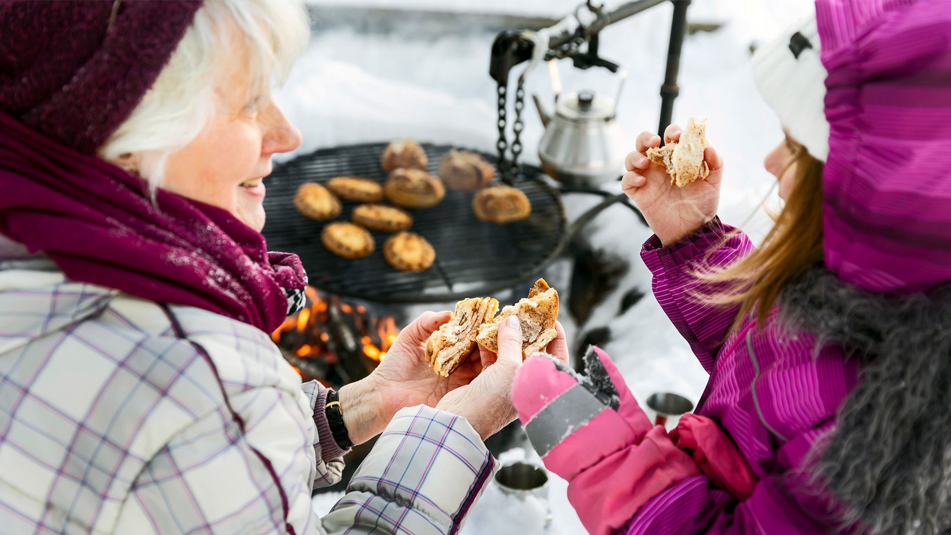 Isoäiti ja tyttö nuotiolla lämmittämässä korvapuusteja