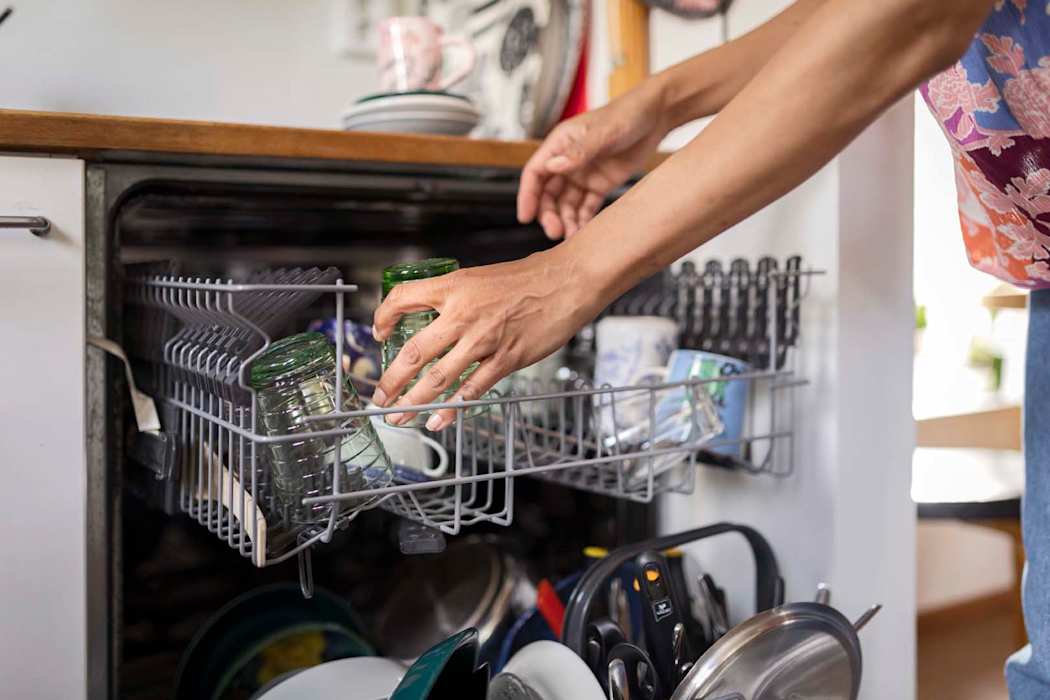 Lähikuva, jossa astianpesukoneesta nostetaan puhtaita astioita pois.