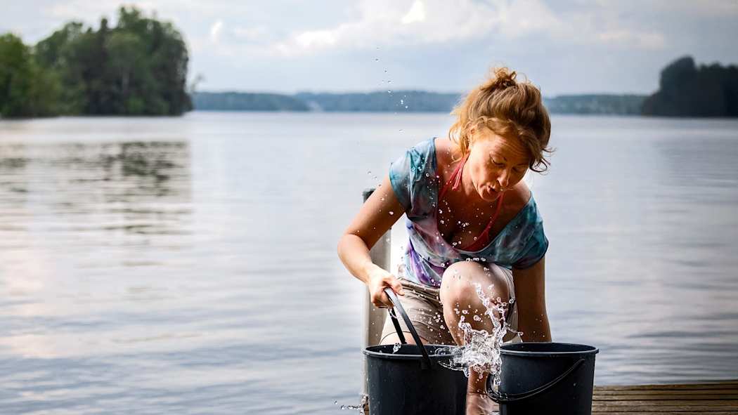 Nainen mökkilaiturilla järvestä vettä hakemassa