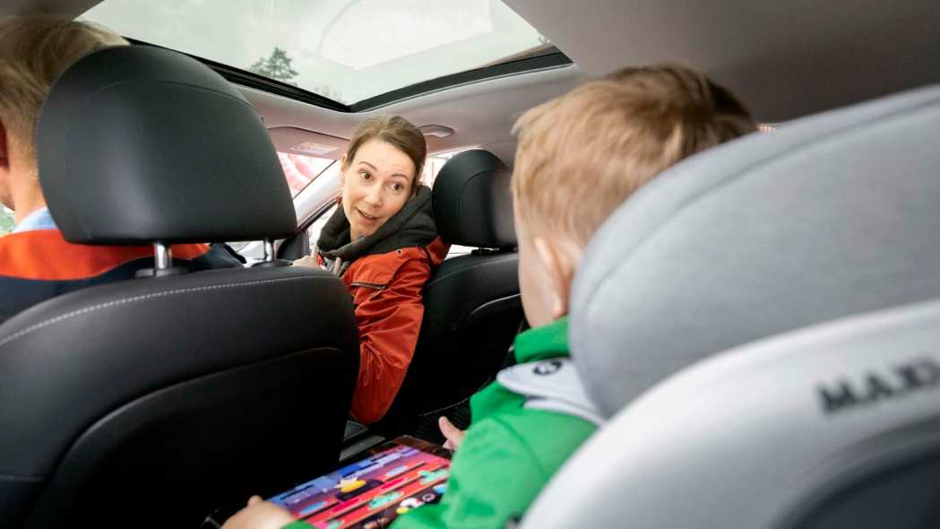 Perhe istuu autossa ja äiti katsoo takapenkillä olevaa lasta.