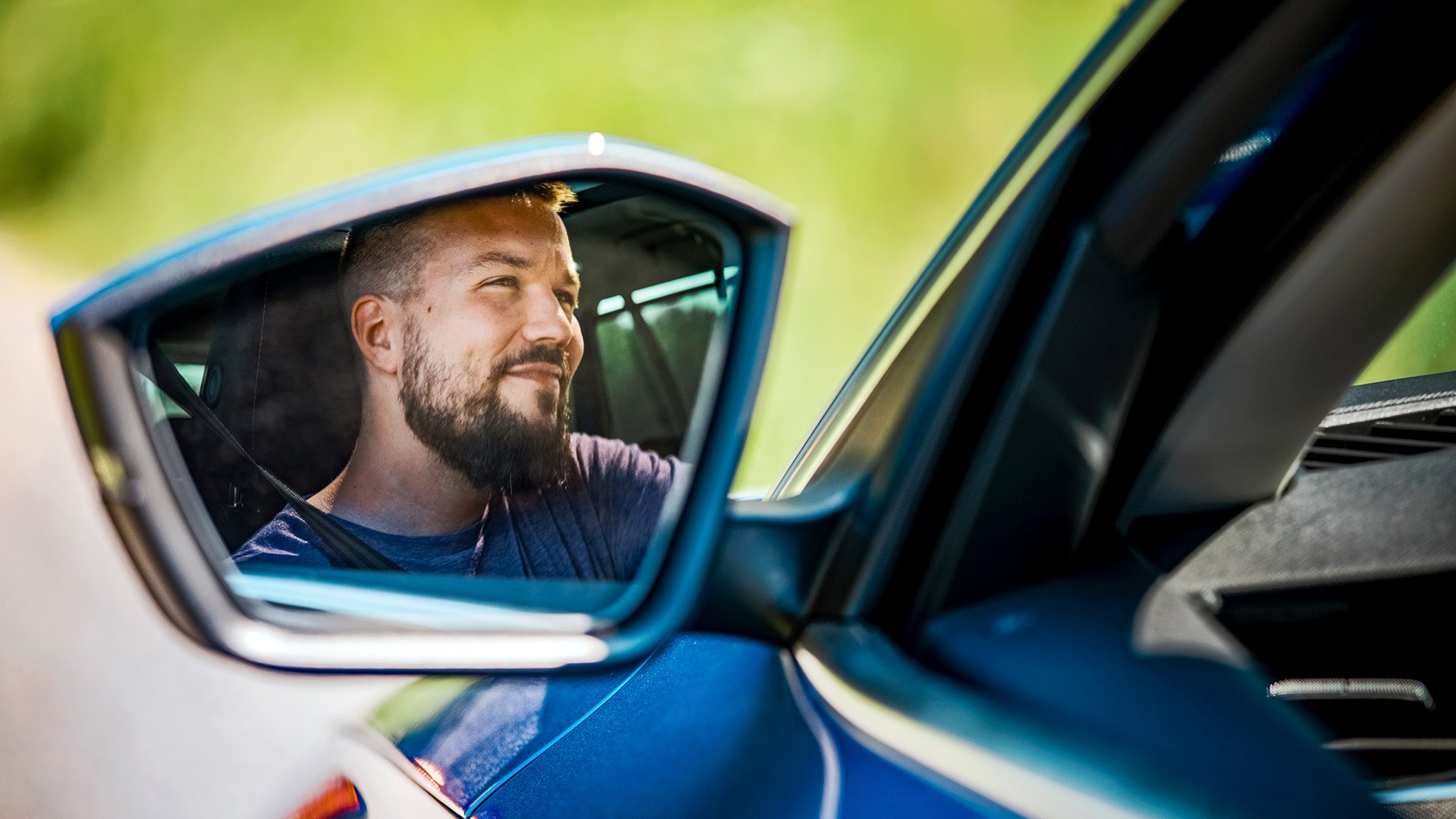 Mies ajaa kesäillassa autoa, kuvakulma sivupeilistä