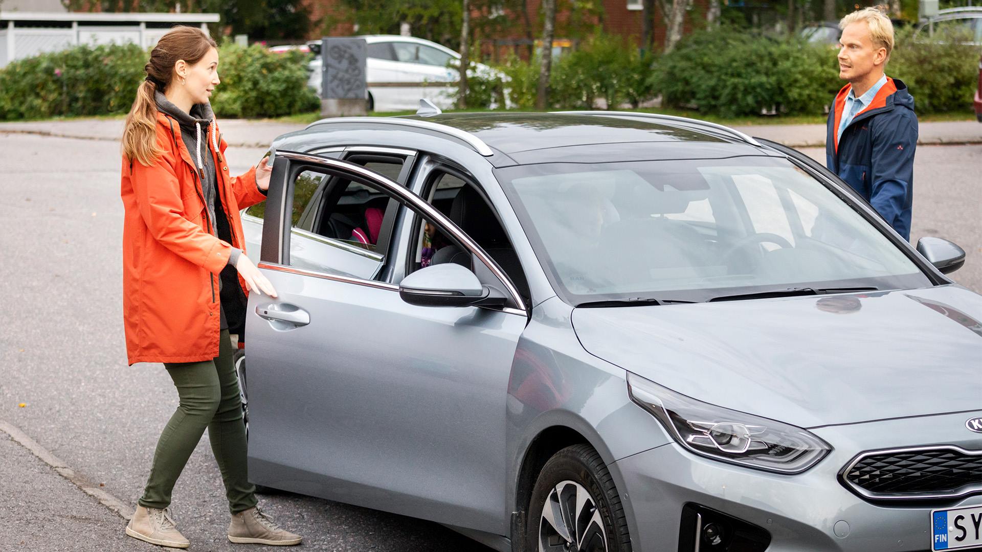 Nainen ja mies nousemassa harmaan henkilöauton kyytiin.