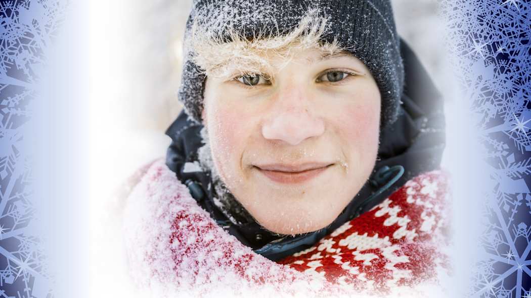 Sinisen lumihiutaletaustan edustalla hymyilee vaaleatukkainen nuori hahmo musta pipo päässä, punavalkoinen kaulahuivi kaulassaan, posket pakkasesta punoittaen ja hymy huulillaan.