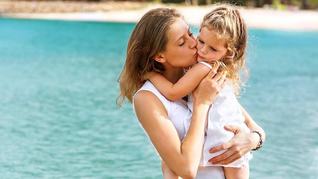 Nainen pitää pientä lasta sylissä rannalla.