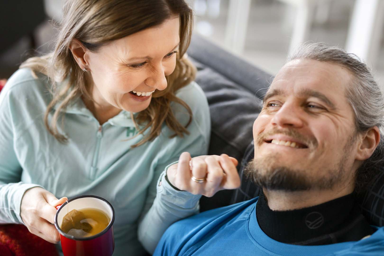 Hymyilevä pariskunta istuu rennosti sohvalla. Naisella on teekuppi kädessä.