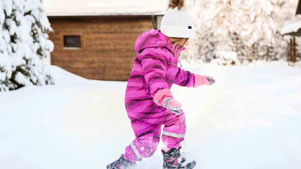 Pieni tyttö juoksee lumessa talvivaatteet päällä.