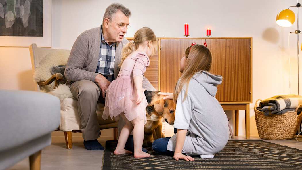 Isoisä ja kaksi lasta rapsuttavat koiraa, taustalla kaksi kynttilää senkin päällä