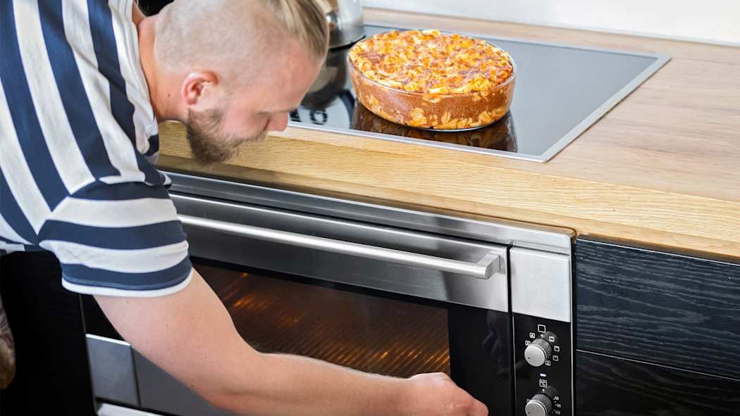 Mies laittamassa uunia pois päältä ruuanlaiton jälkeen