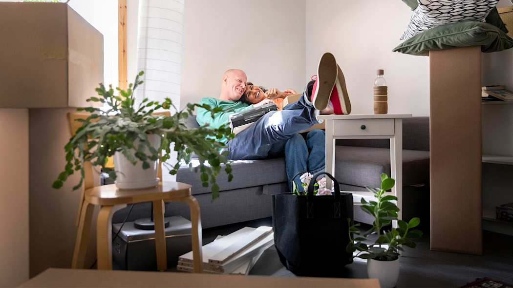 Nainen ja mies istuvat sohvalla muuttolaatikoiden keskellä