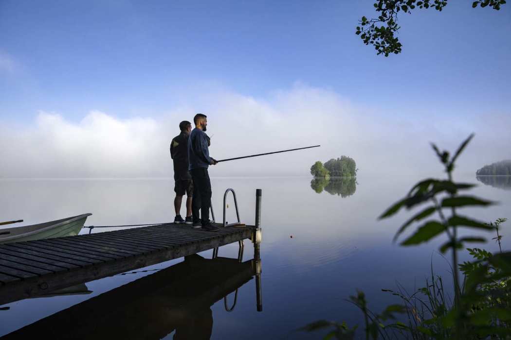Kaksi miestä ongella tyynellä järvellä.