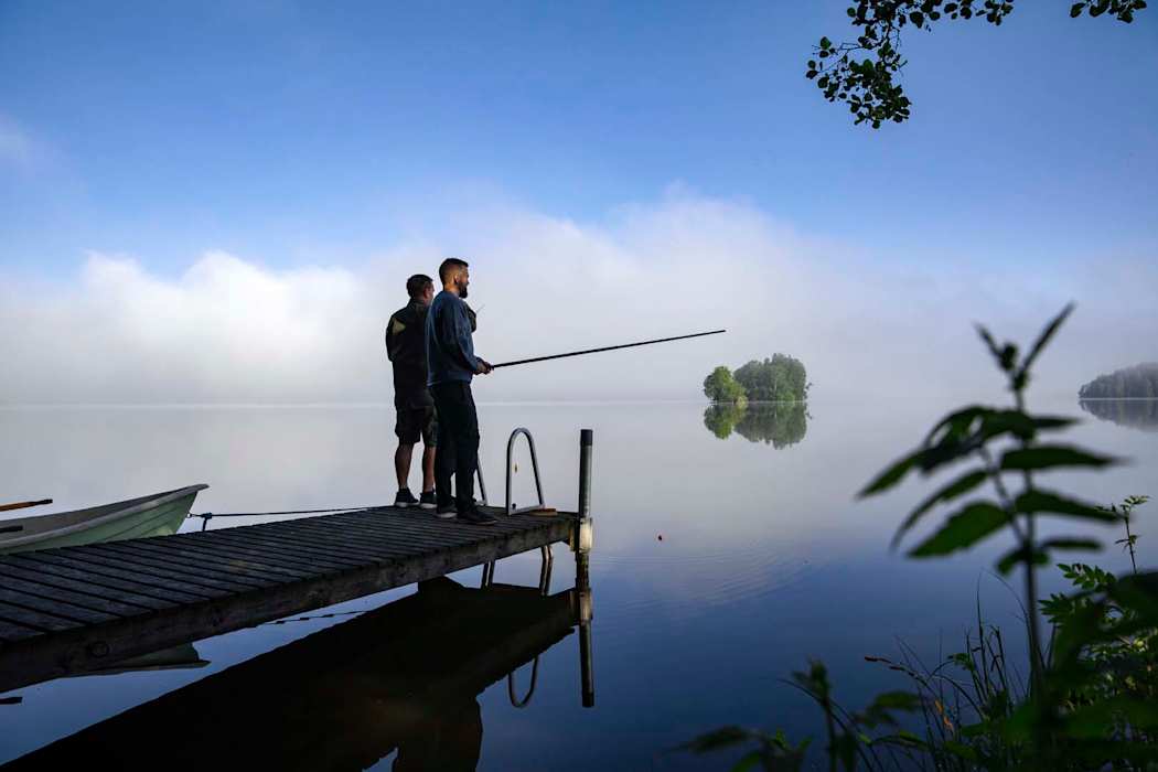 Kaksi miestä ongella tyynellä järvellä.