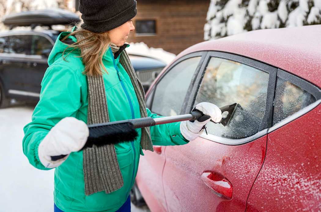 Nainen skrapaa ulkona auton jäistä ikkunaa.