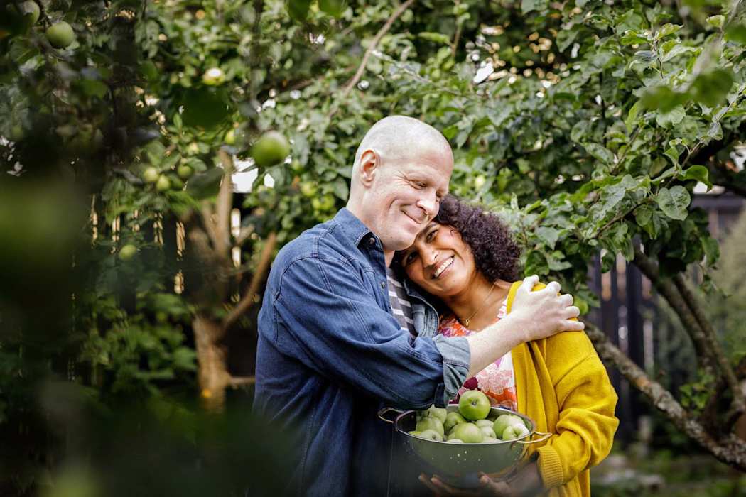 Mies ja nainen halaavat puutarhassa omenavati kädessä
