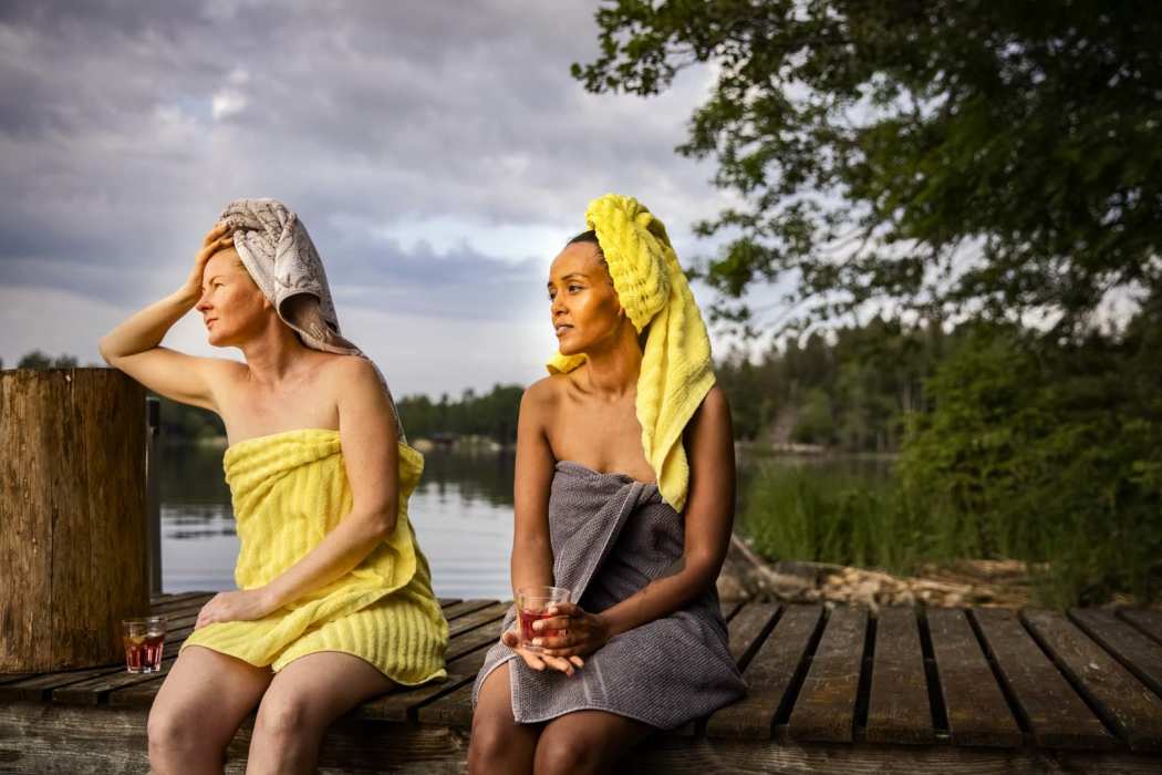 Kaksi naista istuu laiturilla pyyhkeet päällä.