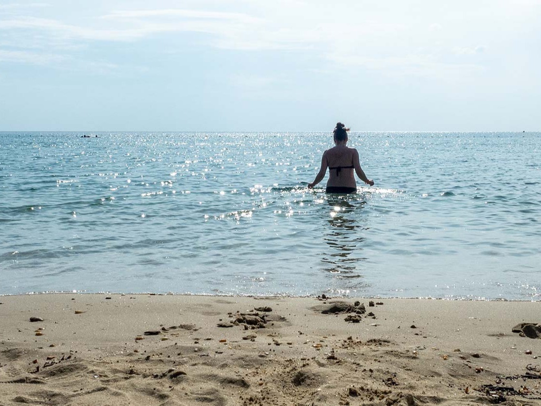 Nainen on menossa uimaan hiekkarannalla auringonpaisteessa.