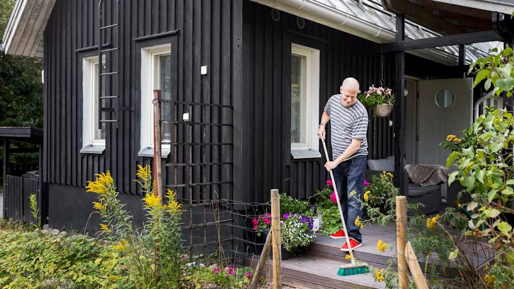 Mies lakaisee terassia omakotitalon edustalla.