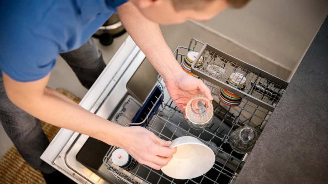 Mies laittaa astioita astianpesukoneeseen.