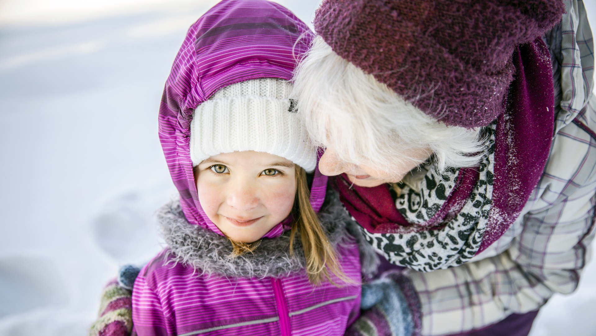 Seniori halaa lasta ulkona talvella.