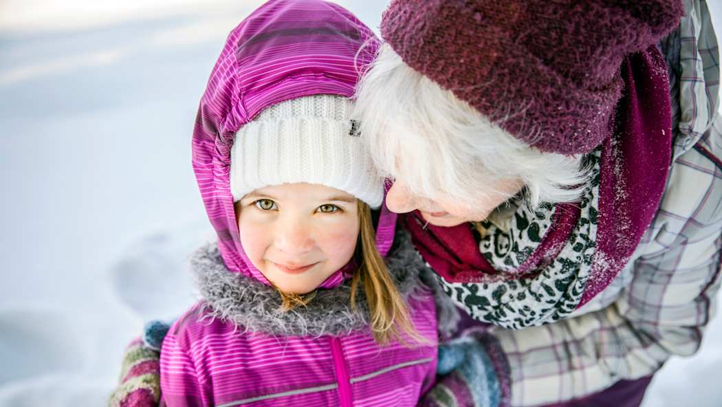 Seniori halaa lasta ulkona talvella.