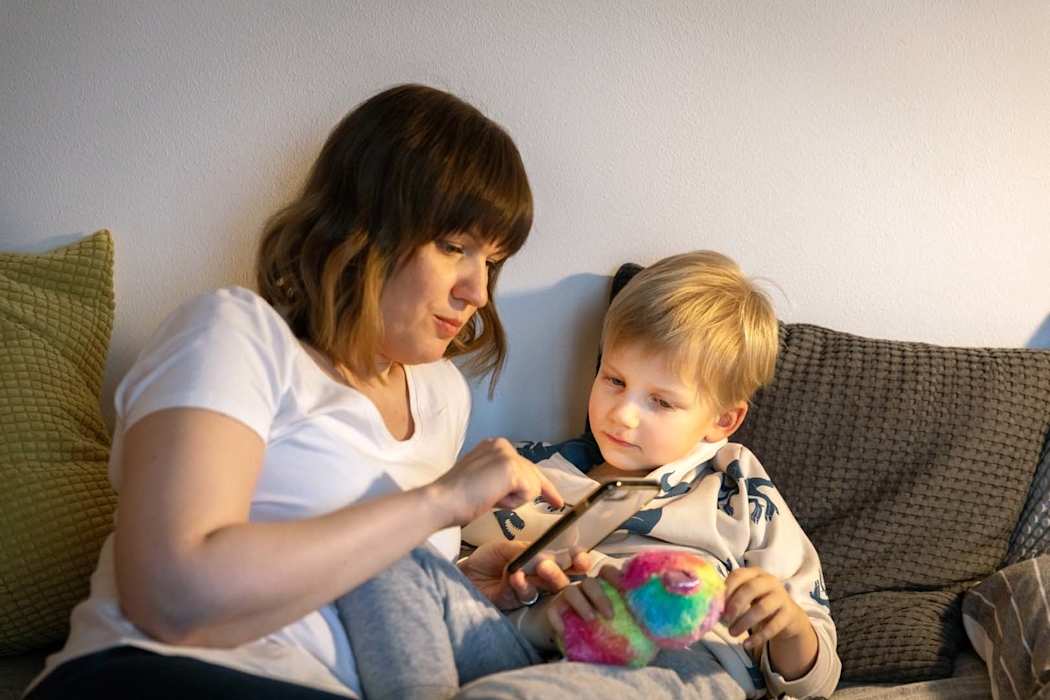 Äiti ja pieni poika istuvat sohvalla ja katsovat puhelinta.