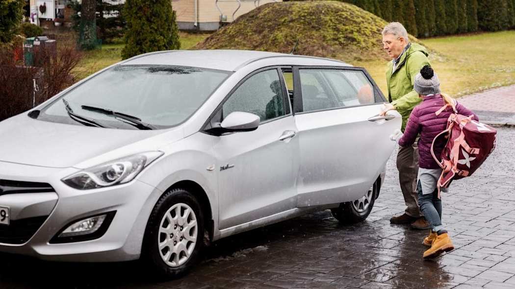 Mies ja lapsi menossa autoon sateisella säällä.